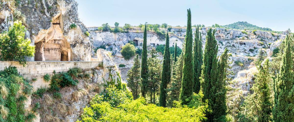 A rocky landscape with a cave-like structure and tall cypress trees.