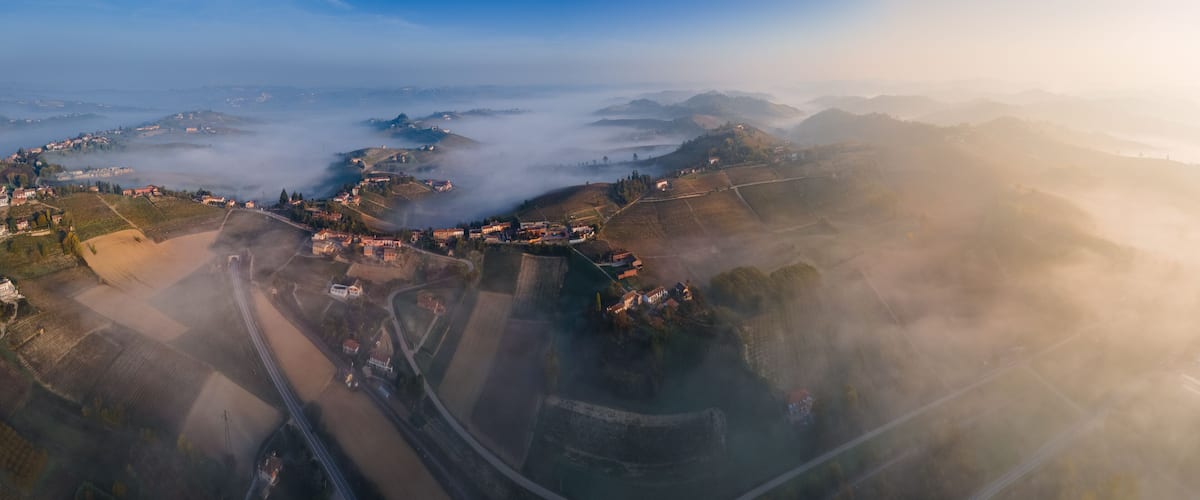 An aerial view of a hilly landscape with a town nestled among the hills, surrounded by fields and roads.