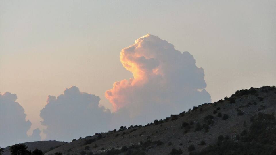 A hill with sparse vegetation and a large cloud formation in the sky.