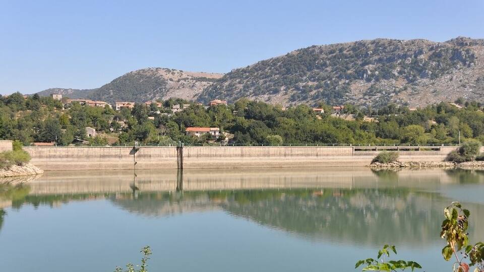 A calm lake with a dam, a bridge, and a mountainous backdrop.