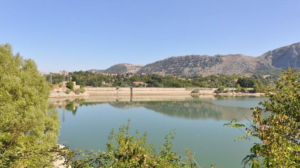 A calm lake with surrounding greenery and mountains in the background.