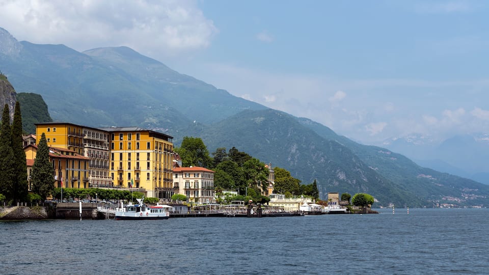 A lakeside town with colorful buildings, a boat docked at the pier, and mountains in the background.