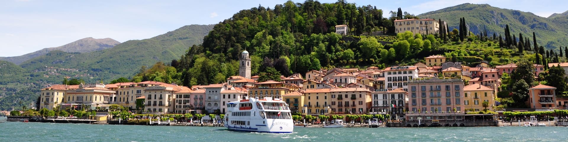 A boat on a lake with a town and mountains in the background.