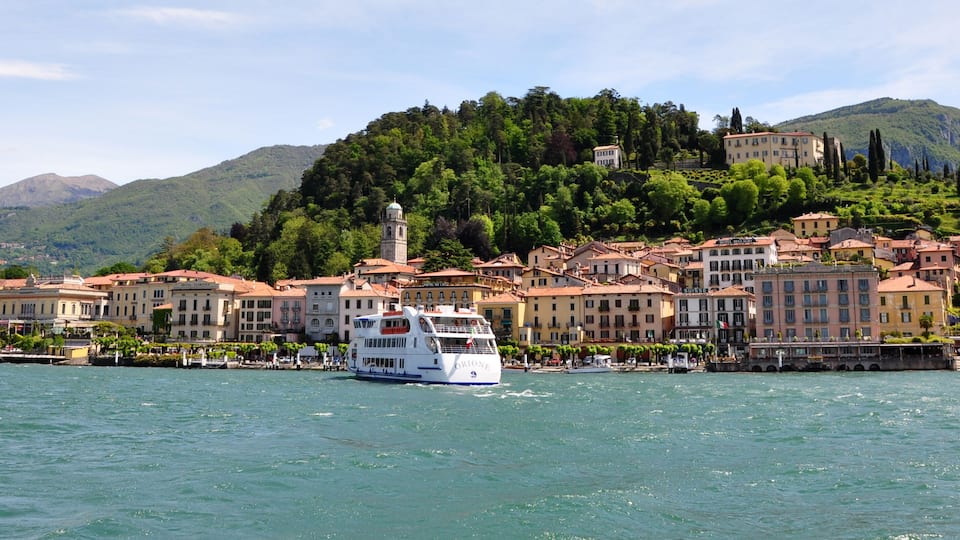 A boat on a lake with a town and mountains in the background.