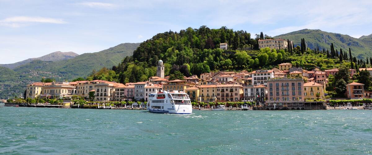 A boat on a lake with a town and mountains in the background.