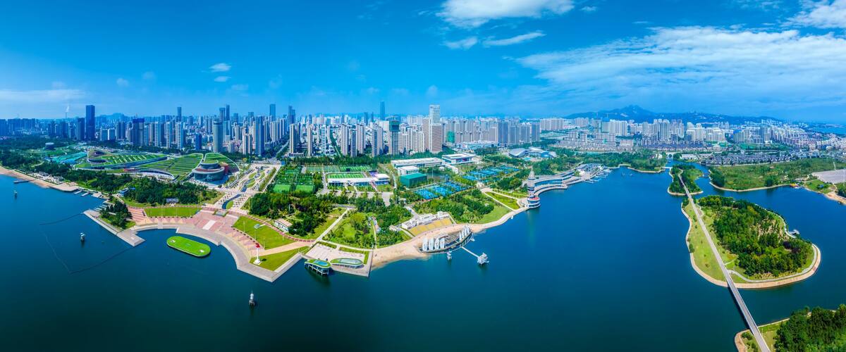 A coastal cityscape with a dense urban skyline, a marina, and a large park area.