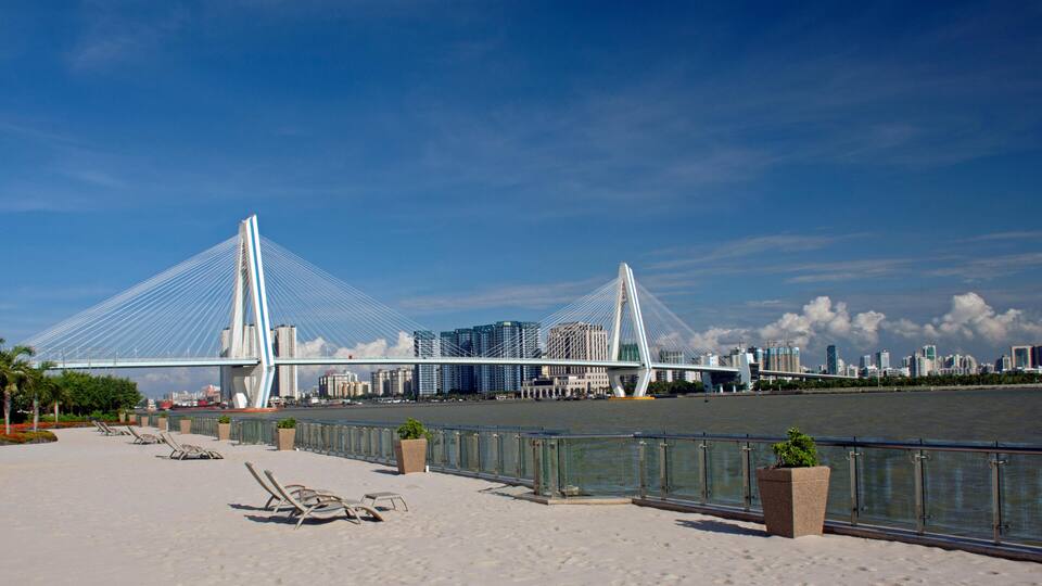 A coastal promenade with beach chairs, a river, and a cable-stayed bridge.