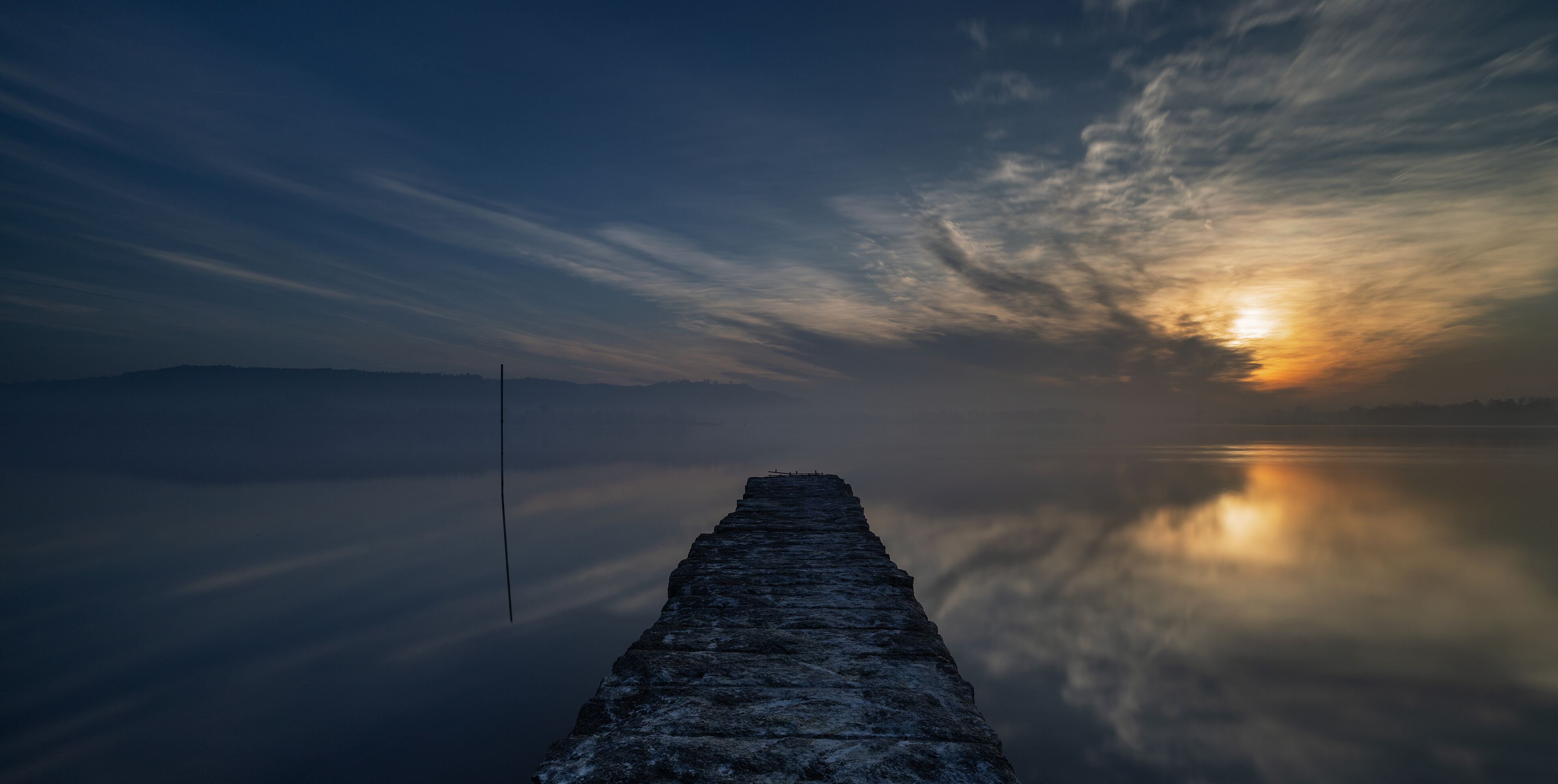 A pier extending into calm waters with a sunset in the background.