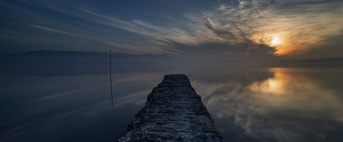 A pier extending into calm waters with a sunset in the background.