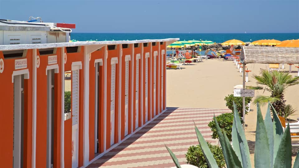 A beach with rows of orange and white buildings, colorful umbrellas, and a clear blue sea.