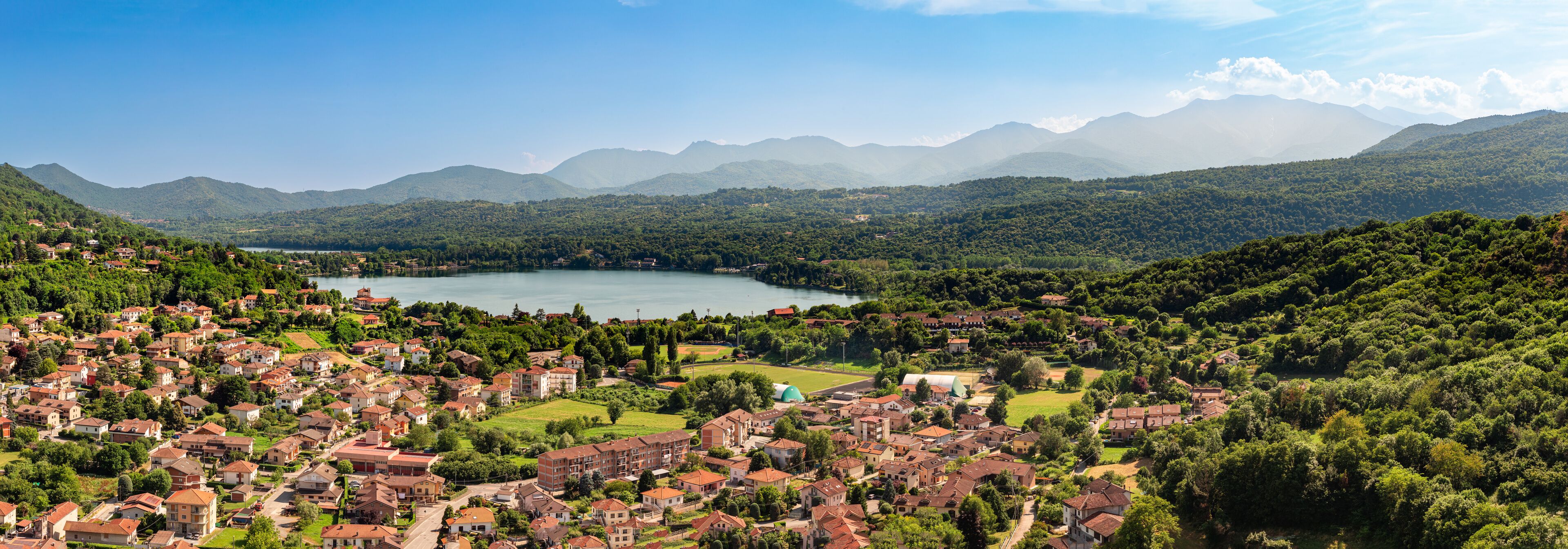 A lake surrounded by mountains and a town with red-roofed houses.