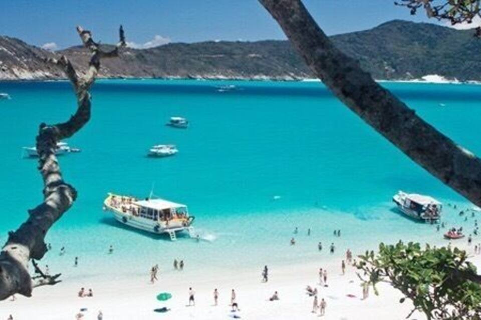 Uma praia com águas turquesa cristalinas, barcos e pessoas.