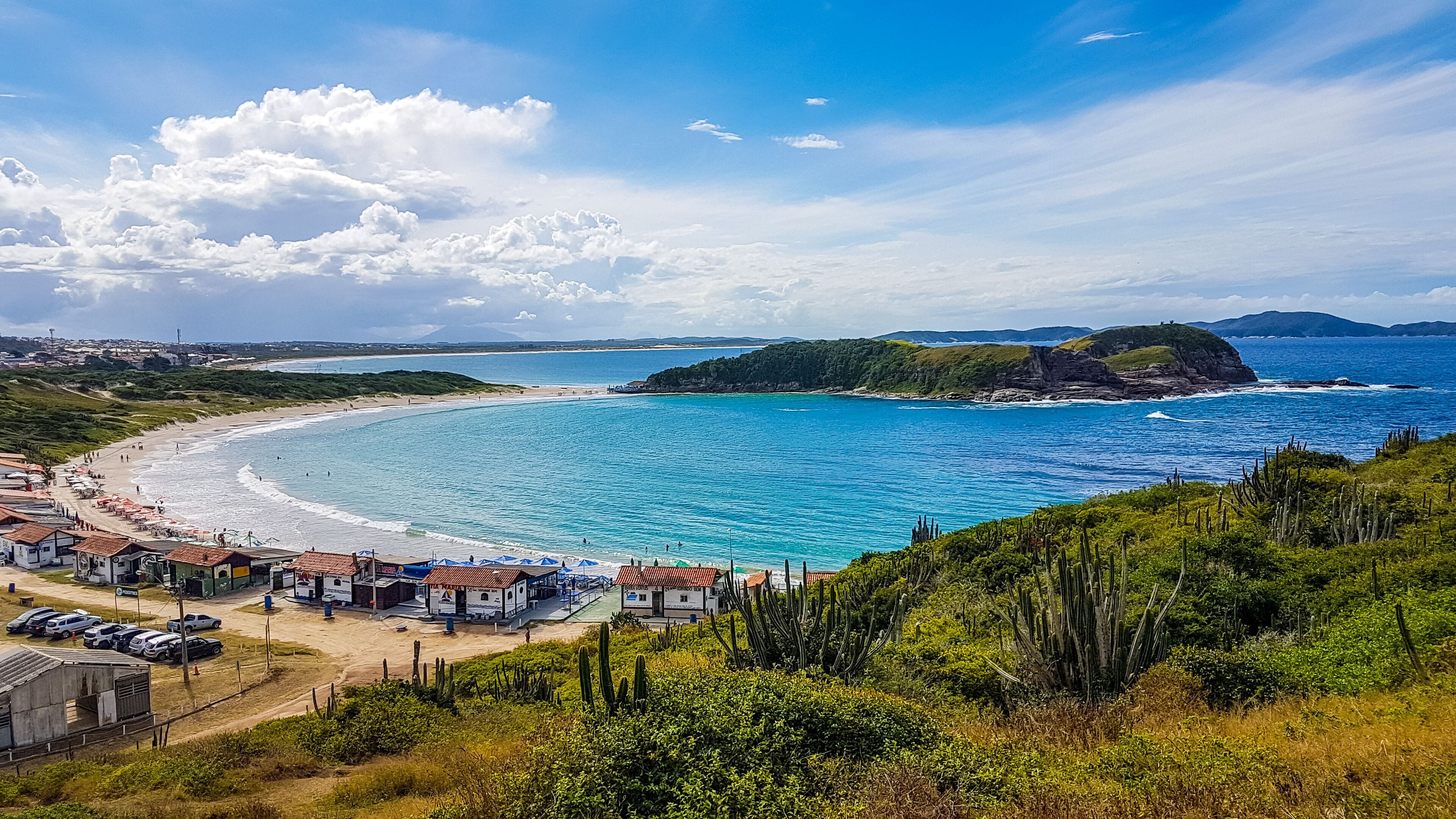 A coastal town with a beach, clear blue waters, and a mountainous backdrop.