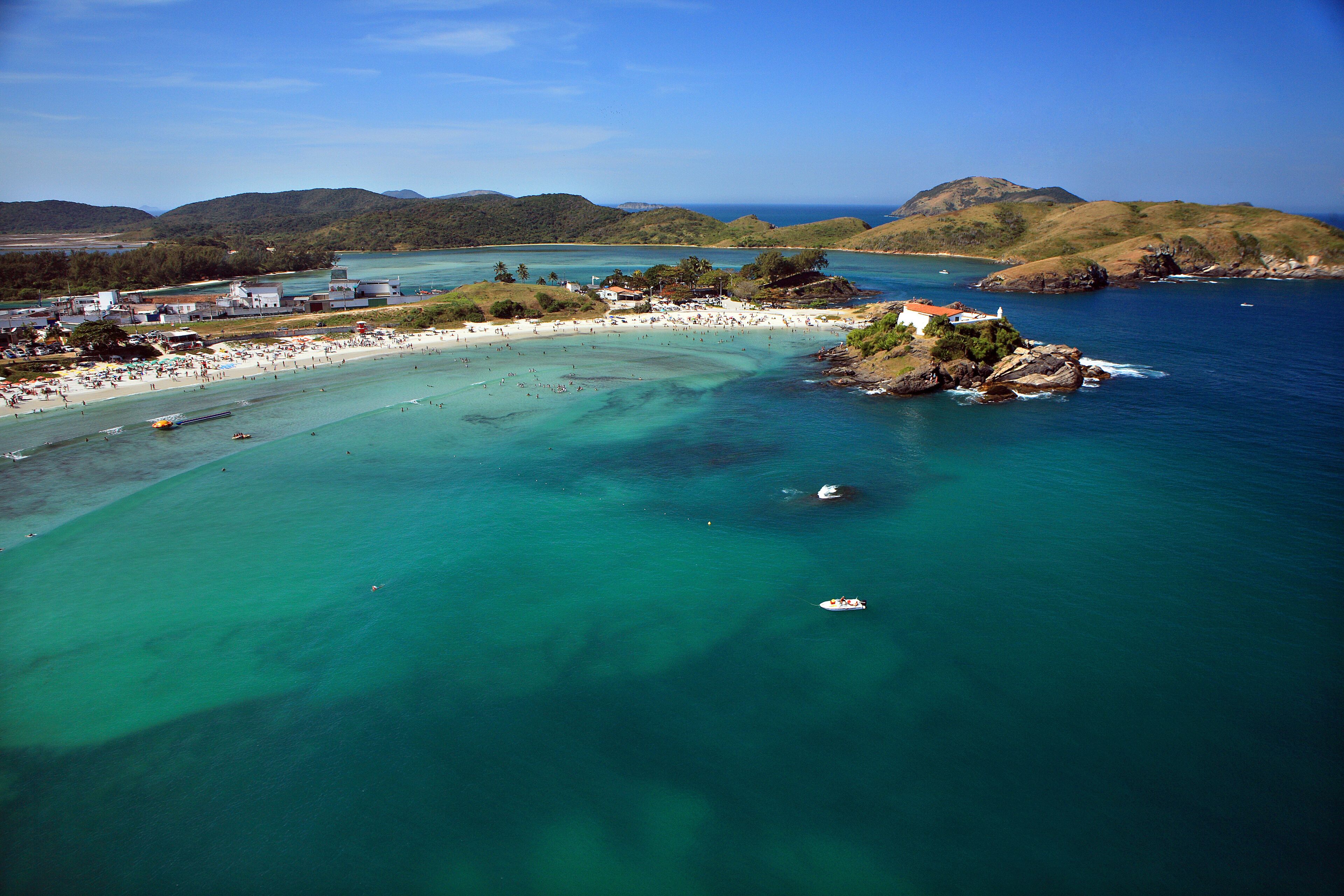A coastal town with a beach, boats, and a mountainous backdrop.