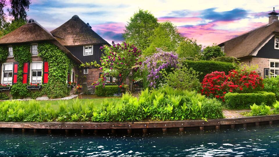 A canal with houses, a wooden bridge, and lush greenery.