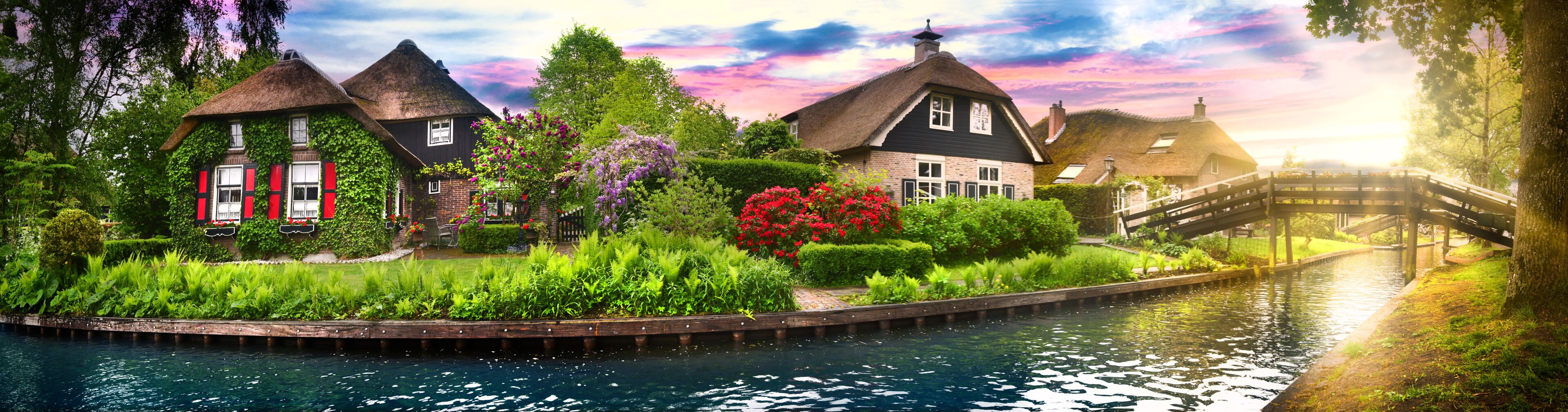 A canal with houses, a wooden bridge, and lush greenery.