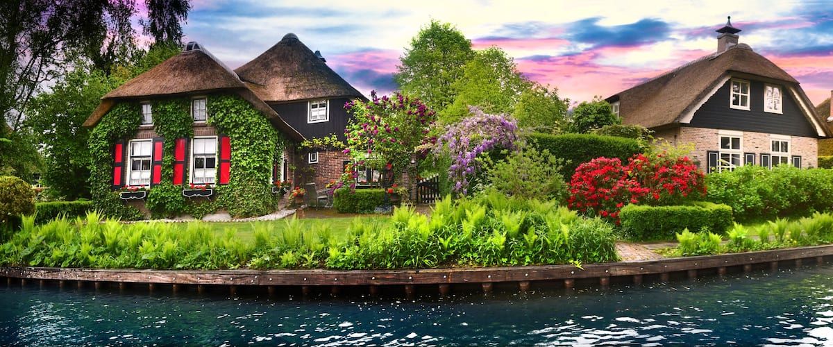 A canal with houses, a wooden bridge, and lush greenery.