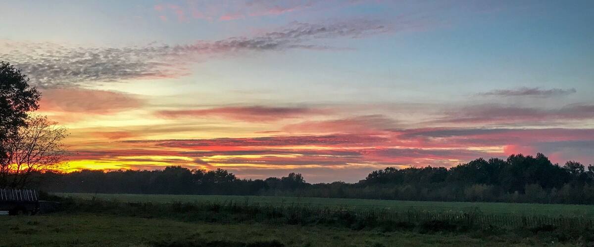 A sunset over a rural landscape with fields and trees.