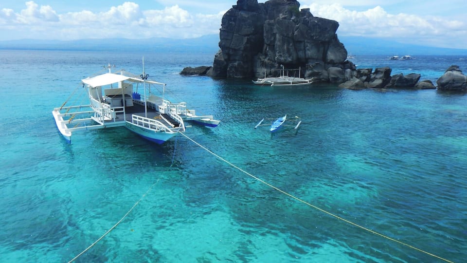 A clear blue sea with boats anchored near a rocky outcrop.