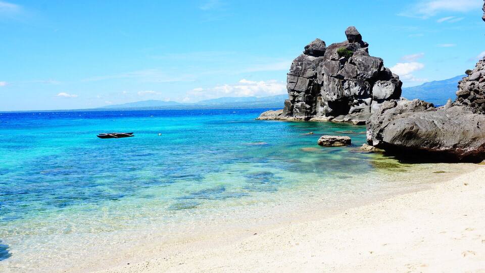 A clear turquoise sea, a sandy beach, and rocky formations.