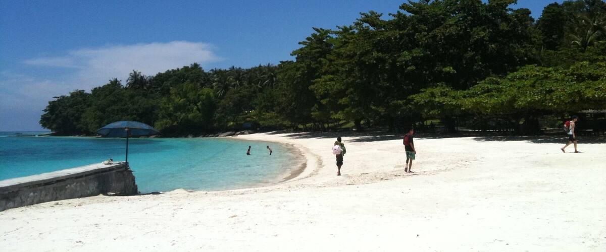 A beach with clear turquoise water, white sand, and lush green trees in the background.