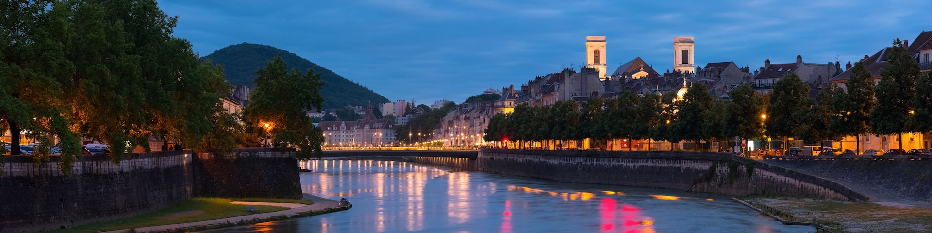 A river reflecting city lights, a bridge, and historic buildings with towers.