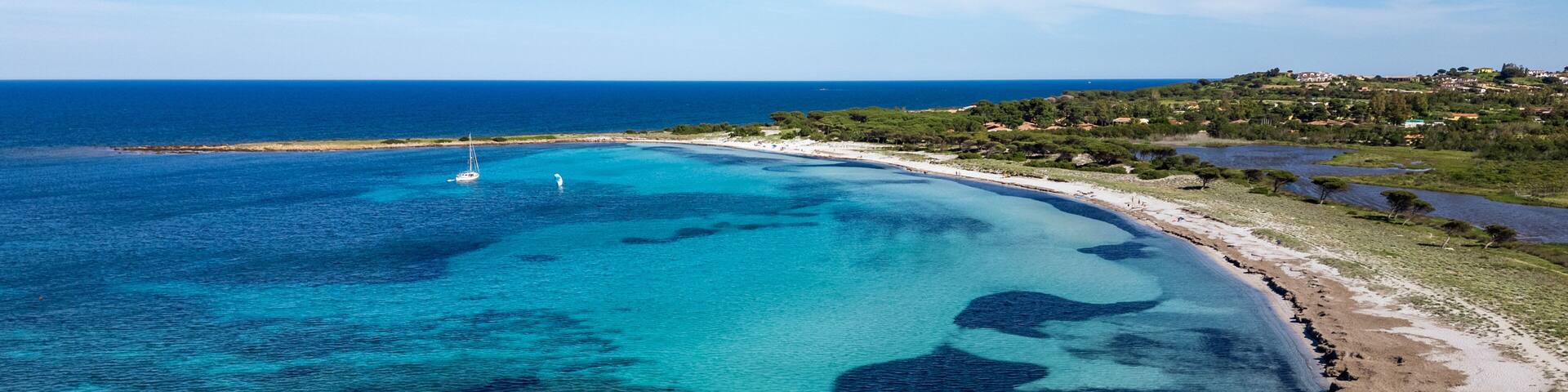 Aerial view of Porto Ainu beach with pine forest and crystal clear waters, Budoni, Sardinia.