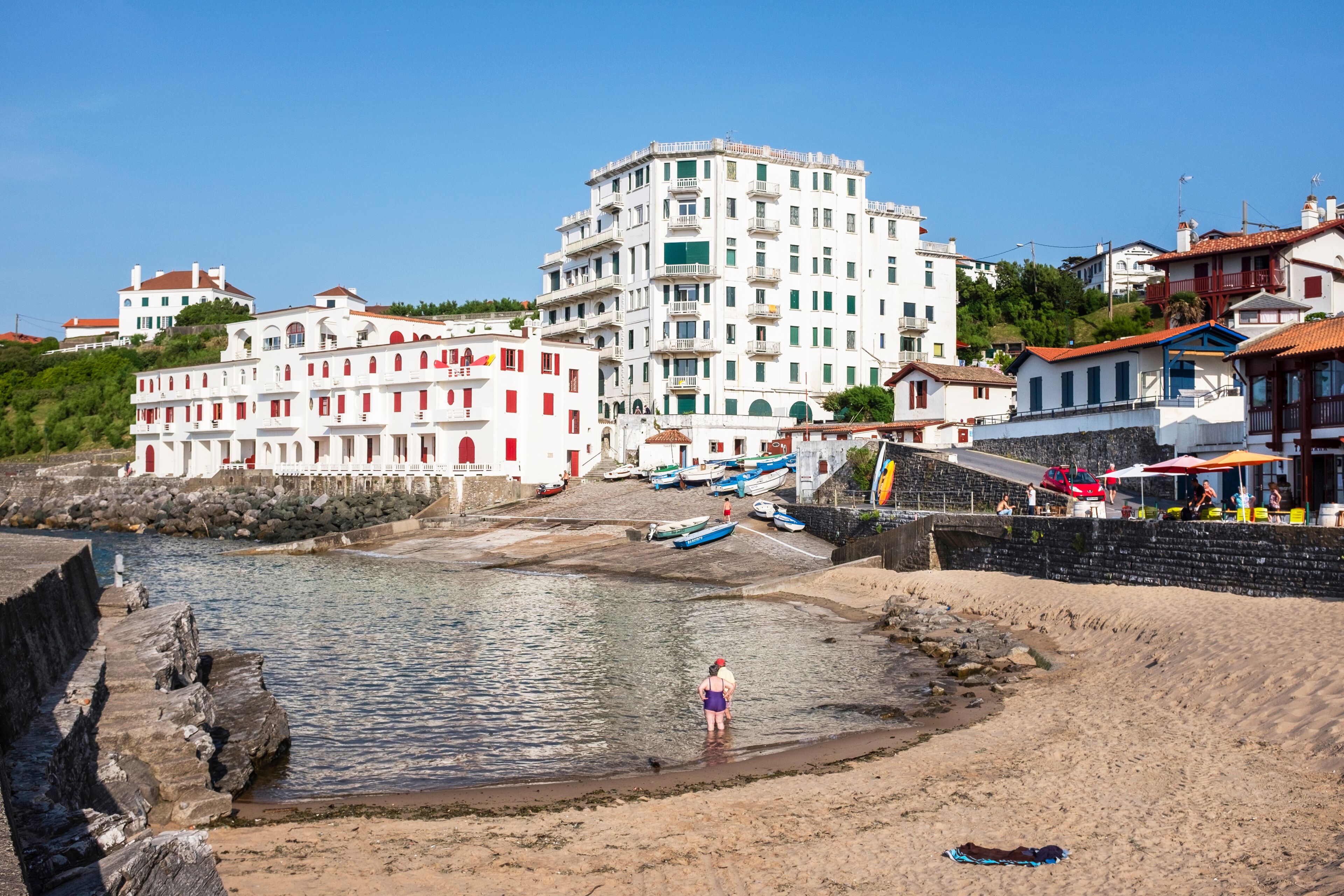 A coastal town with a prominent white building, a sandy beach, and boats docked near the shore.