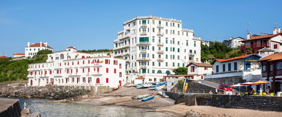 A coastal town with a prominent white building, a sandy beach, and boats docked near the shore.