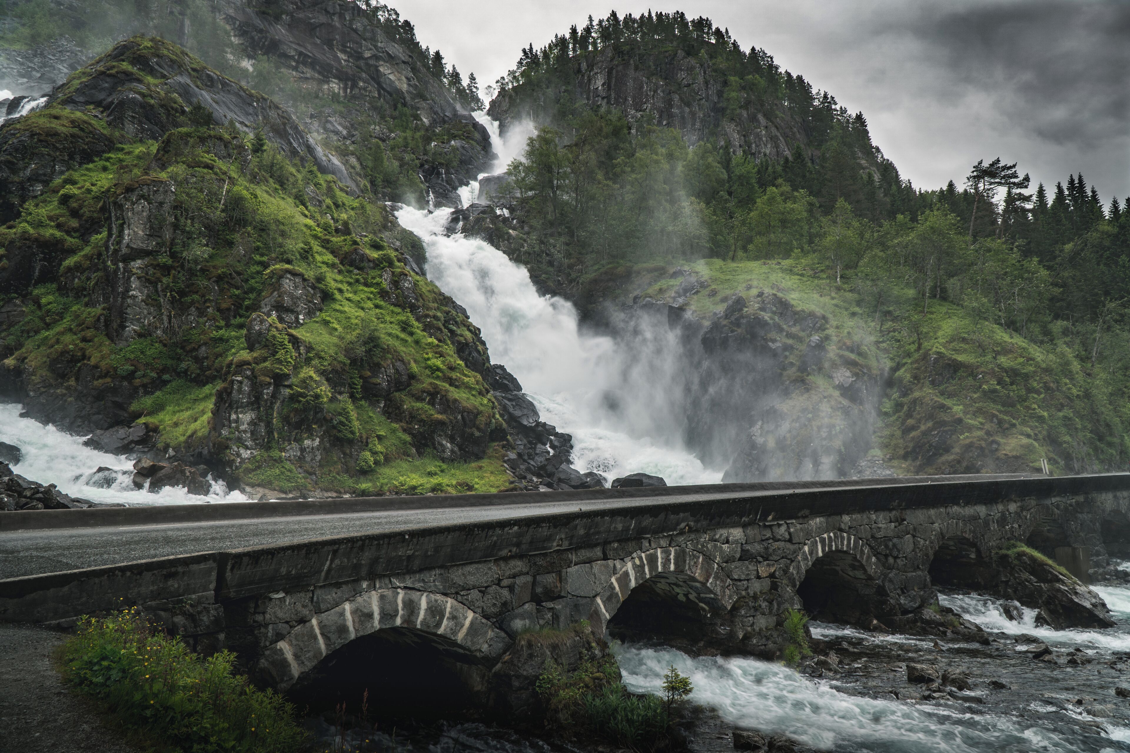 A stone bridge over a river with a waterfall in the background.