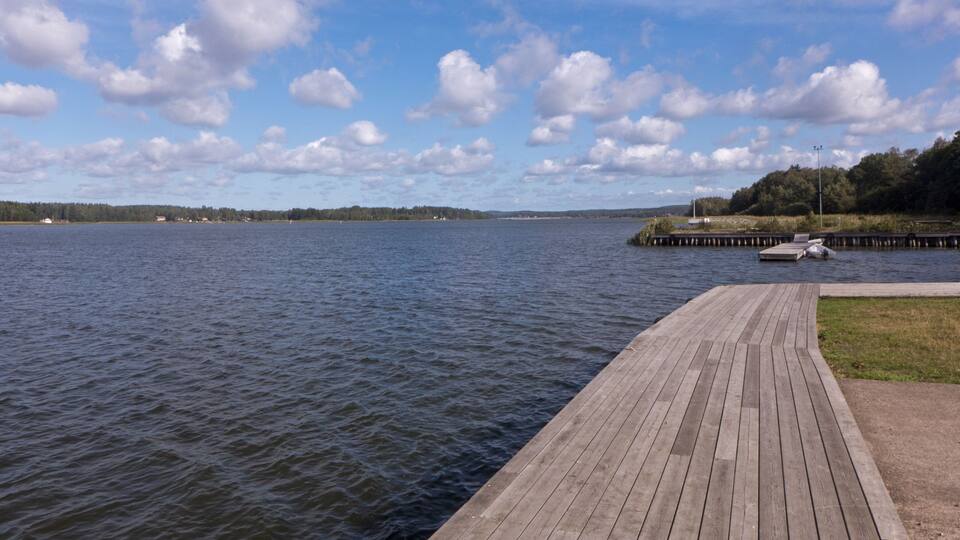 A wooden pier extending into a calm lake with a clear sky and scattered clouds.