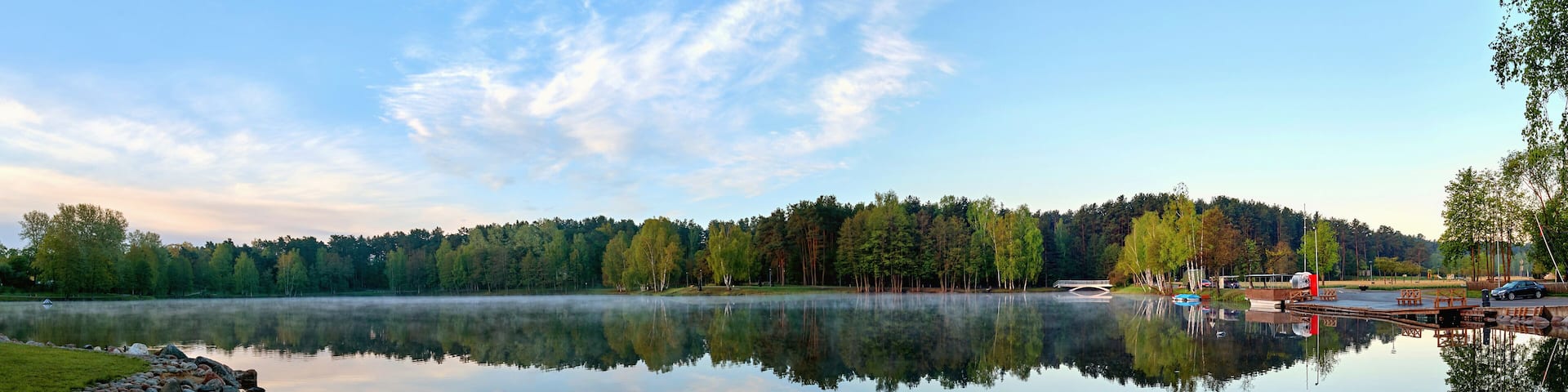 A calm lake with a rocky shoreline, surrounded by dense forest and a clear sky.