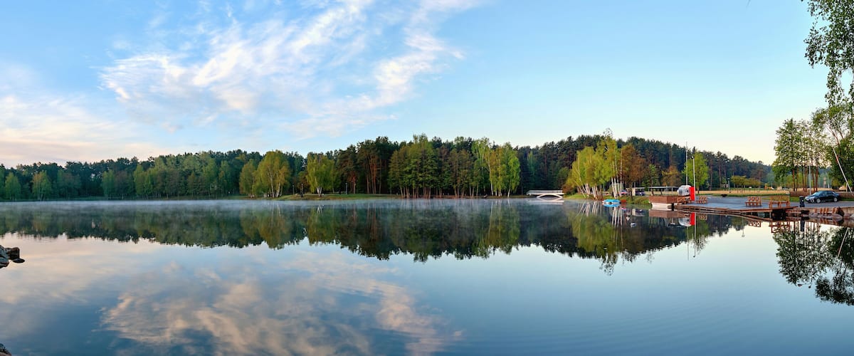 A calm lake with a rocky shoreline, surrounded by dense forest and a clear sky.