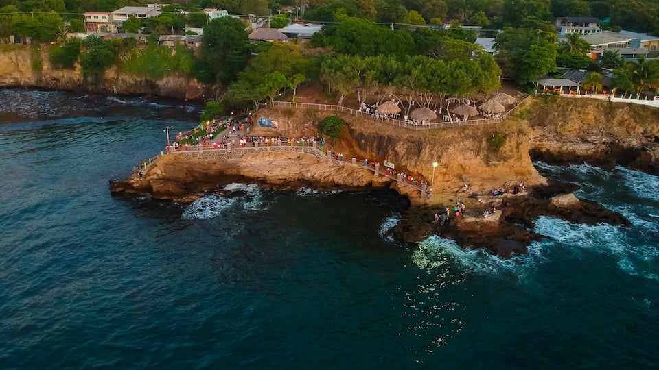 A coastal cliff with a viewing platform, a beach, and a town in the background.