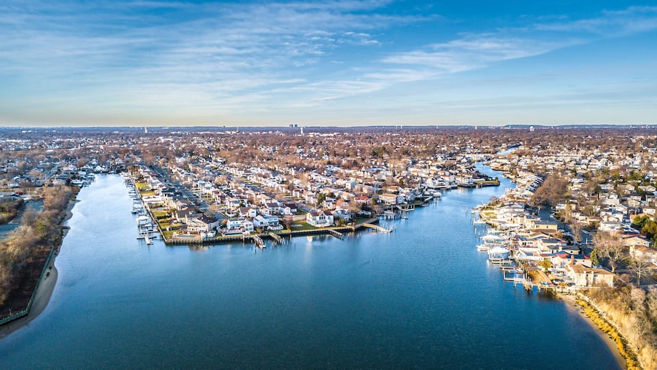 An aerial view of a river town with a dense residential area, docks, and a distant landmark.