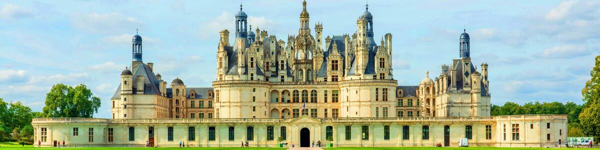 A grand, ornate palace with multiple towers and domes, surrounded by well-maintained lawns and a clear sky.