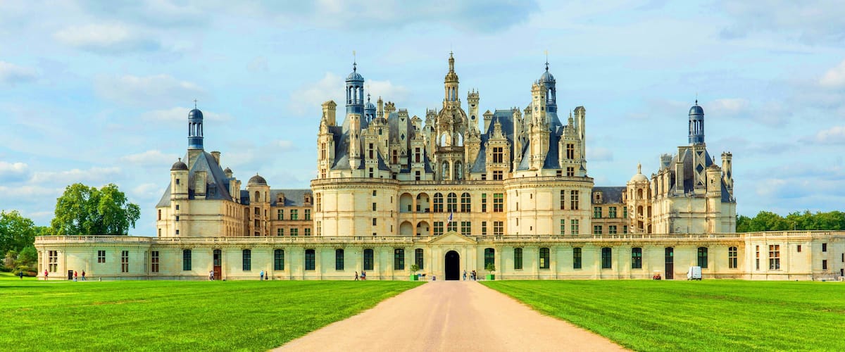 A grand, ornate palace with multiple towers and domes, surrounded by well-maintained lawns and a clear sky.