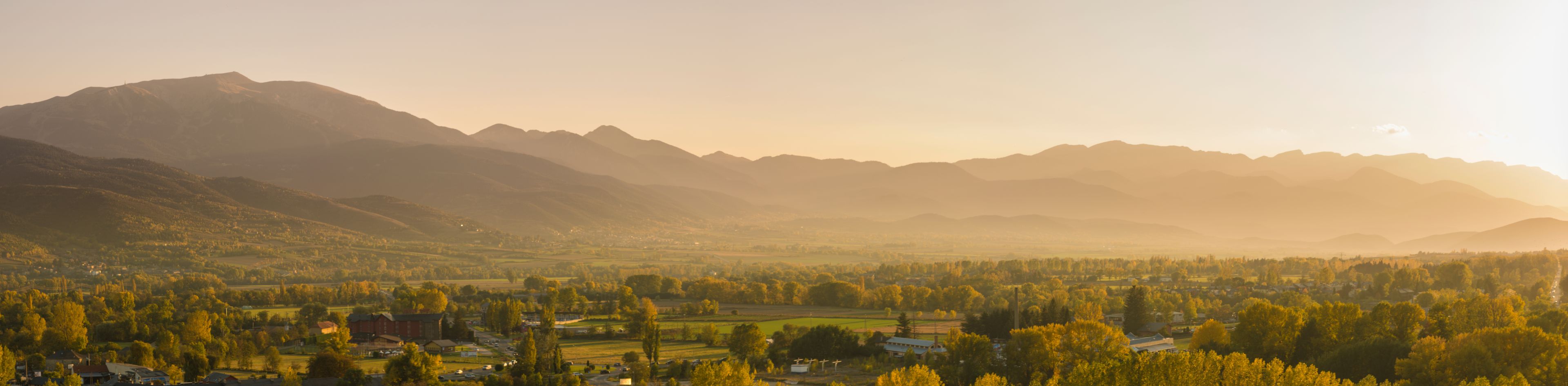 Une vallée avec des montagnes en arrière-plan et une ville au premier plan.