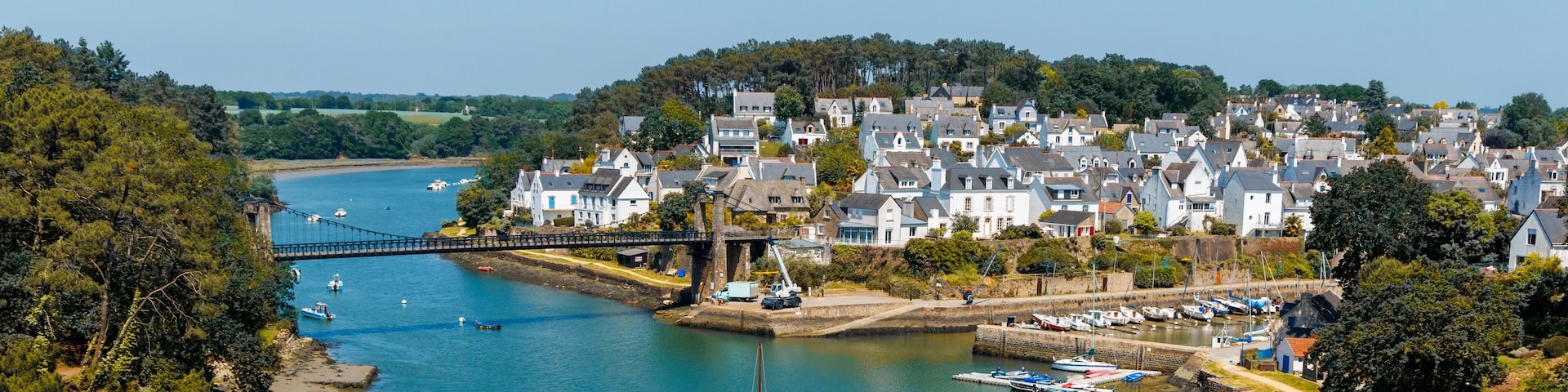 Une riviĂšre avec un pont, un voilier et une ville avec des maisons et des bateaux.