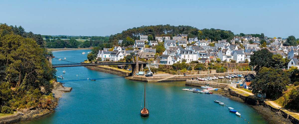A river with a bridge, a sailboat, and a town with houses and boats.
