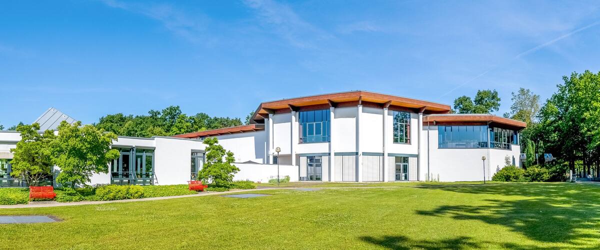 A modern two-story house with a red roof, surrounded by a well-maintained lawn and trees.