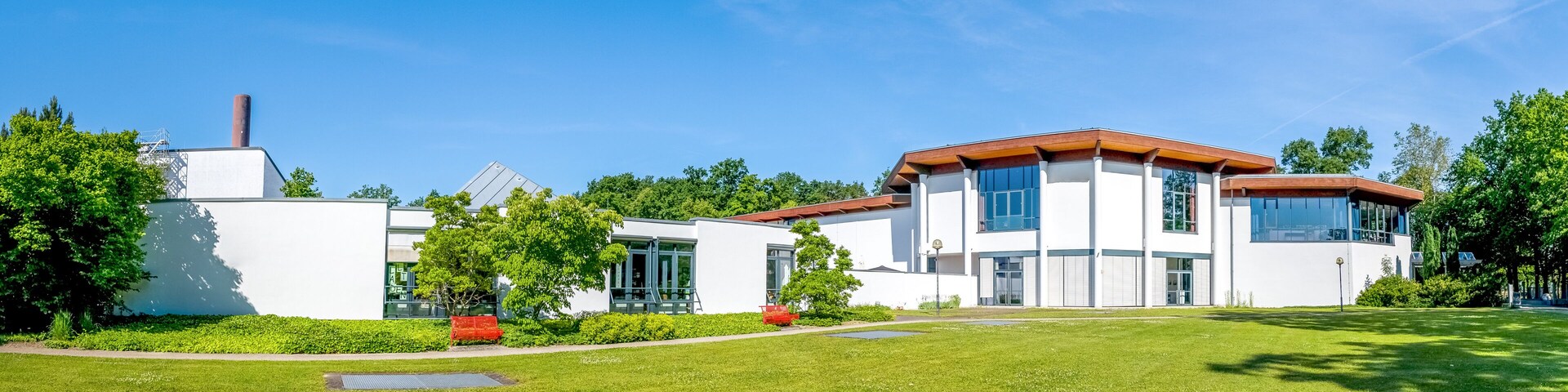 A modern two-story house with a red roof, surrounded by a well-maintained lawn and trees.