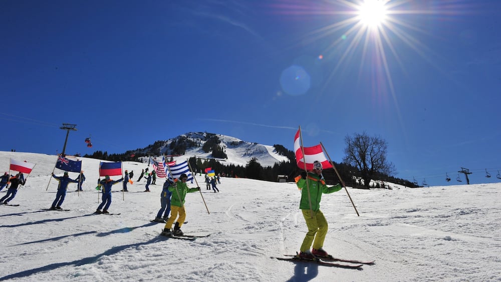 Des skieurs sur une pente enneigée, avec des drapeaux, un ciel bleu dégagé et une montagne en arrière-plan.