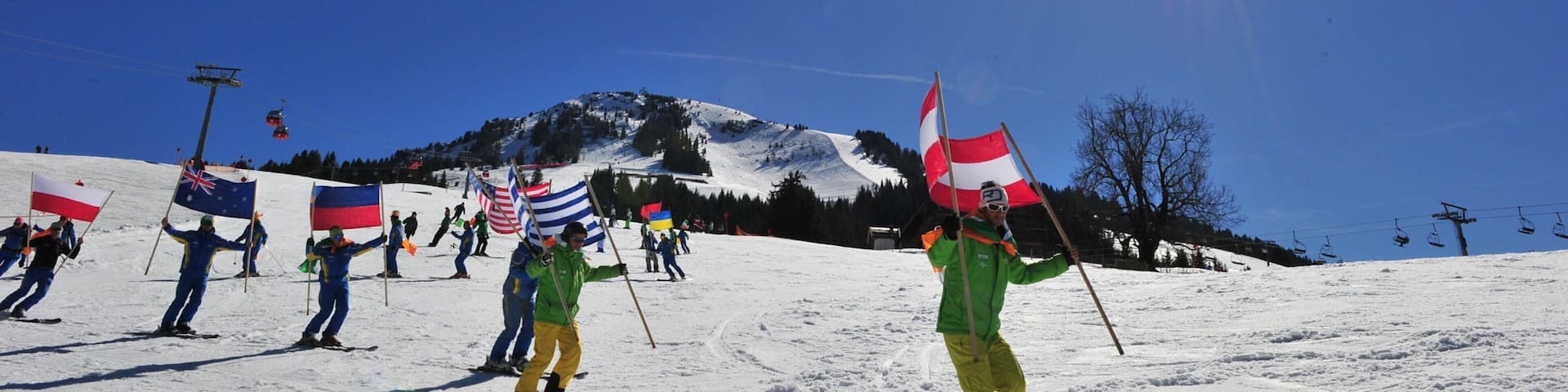 Skiers on a snowy slope with flags, a clear blue sky, and a mountain in the background.