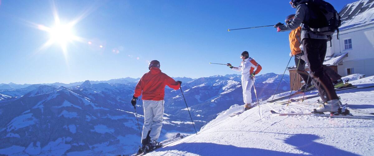 Three skiers on a snowy mountain slope with a clear blue sky and sun shining.