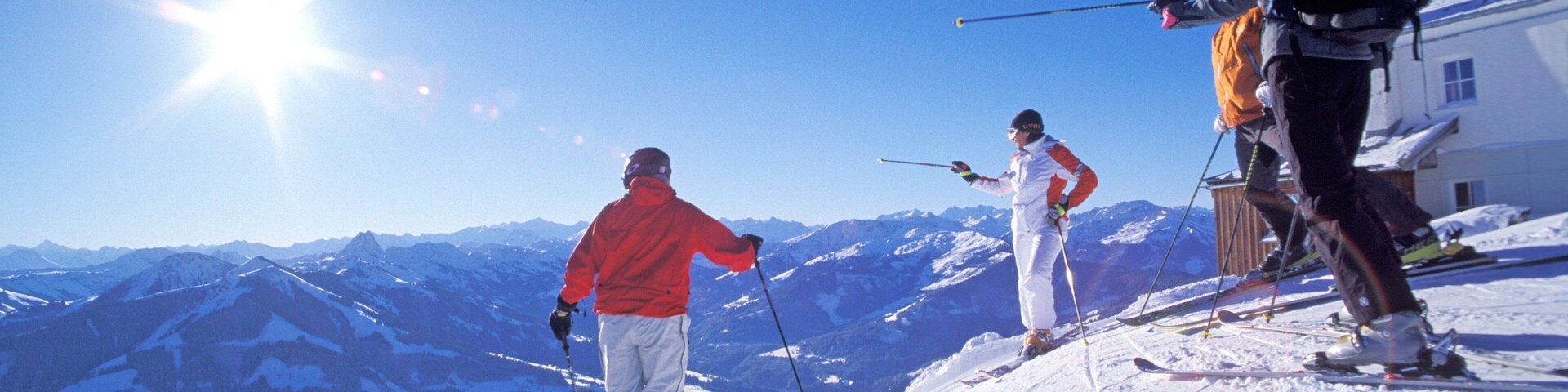 Three skiers on a snowy mountain slope with a clear blue sky and sun shining.