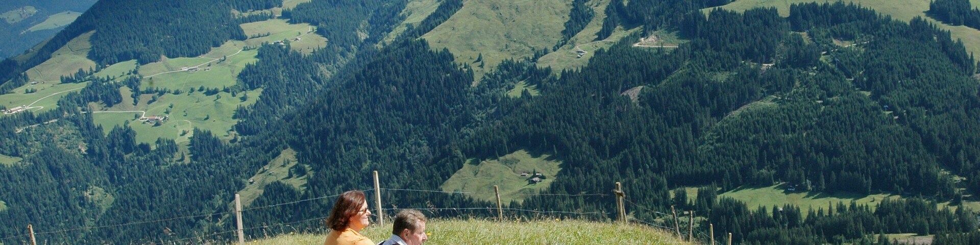 Una familia sentada en una colina cubierta de hierba, con un paisaje montañoso al fondo.
