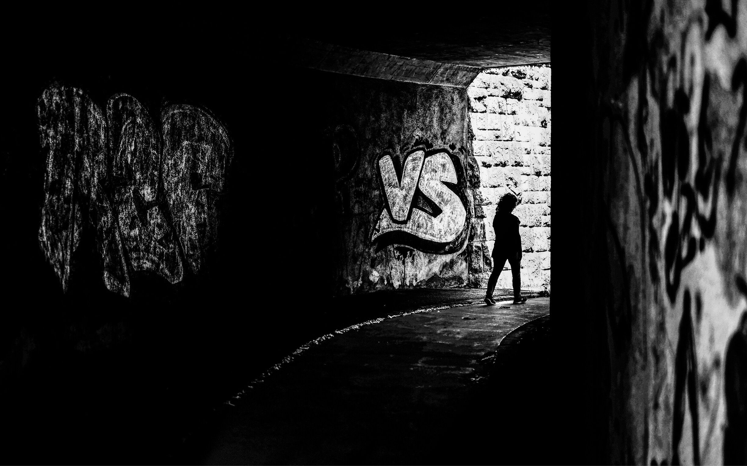 A person standing in a dimly lit tunnel with graffiti on the walls.