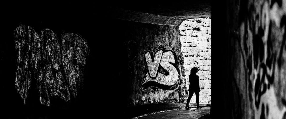 A person standing in a dimly lit tunnel with graffiti on the walls.