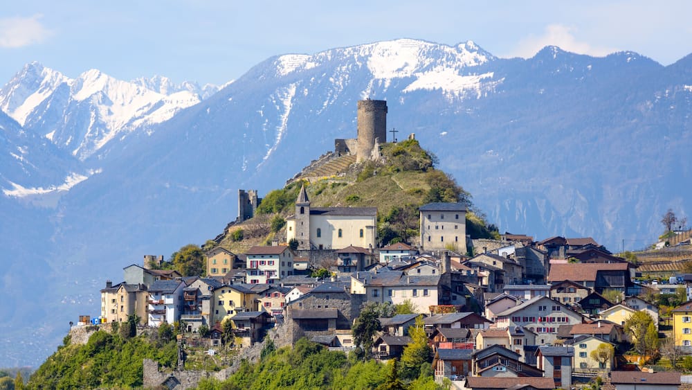 A mountainous village with historic stone buildings and a prominent tower on a hill.